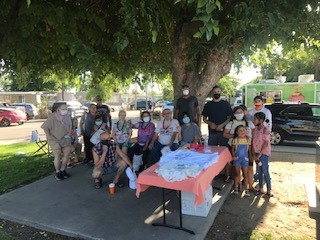 Residents pose for photo behind a pic Nic table at an outdoor community engagement event