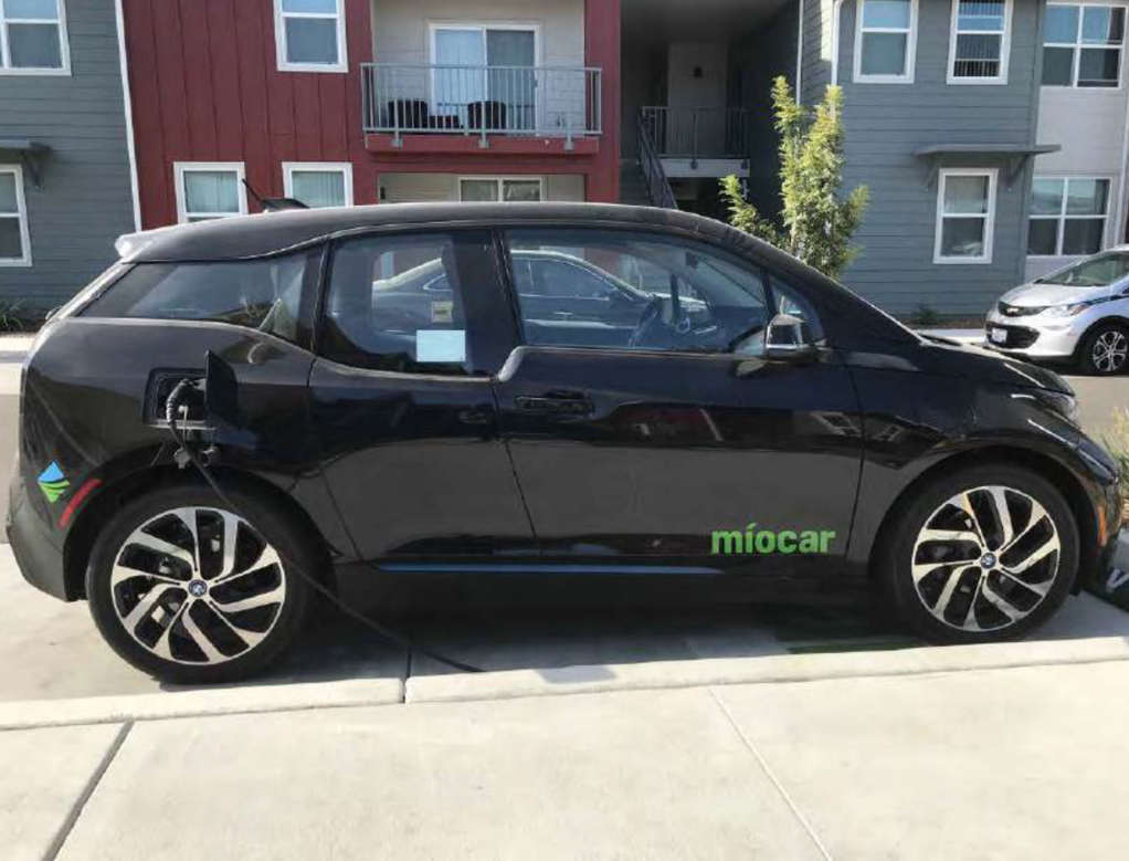 Black Chevy Bolt with Miocar Logo on door parked along a sidewalk