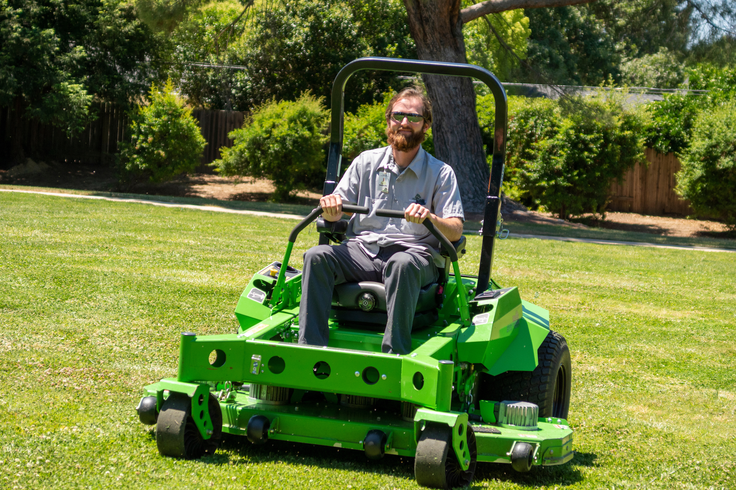 Man driving zero-emission, ride-around lawn mower on green grass