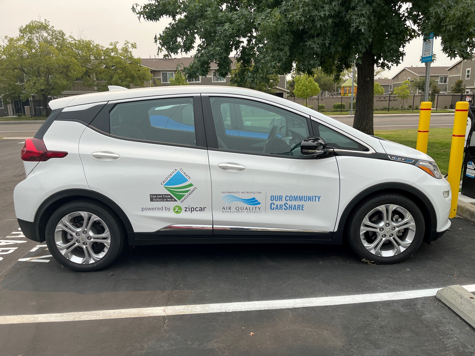 Side view of parked, white Chevy Bolt with Our Community Carshare logo