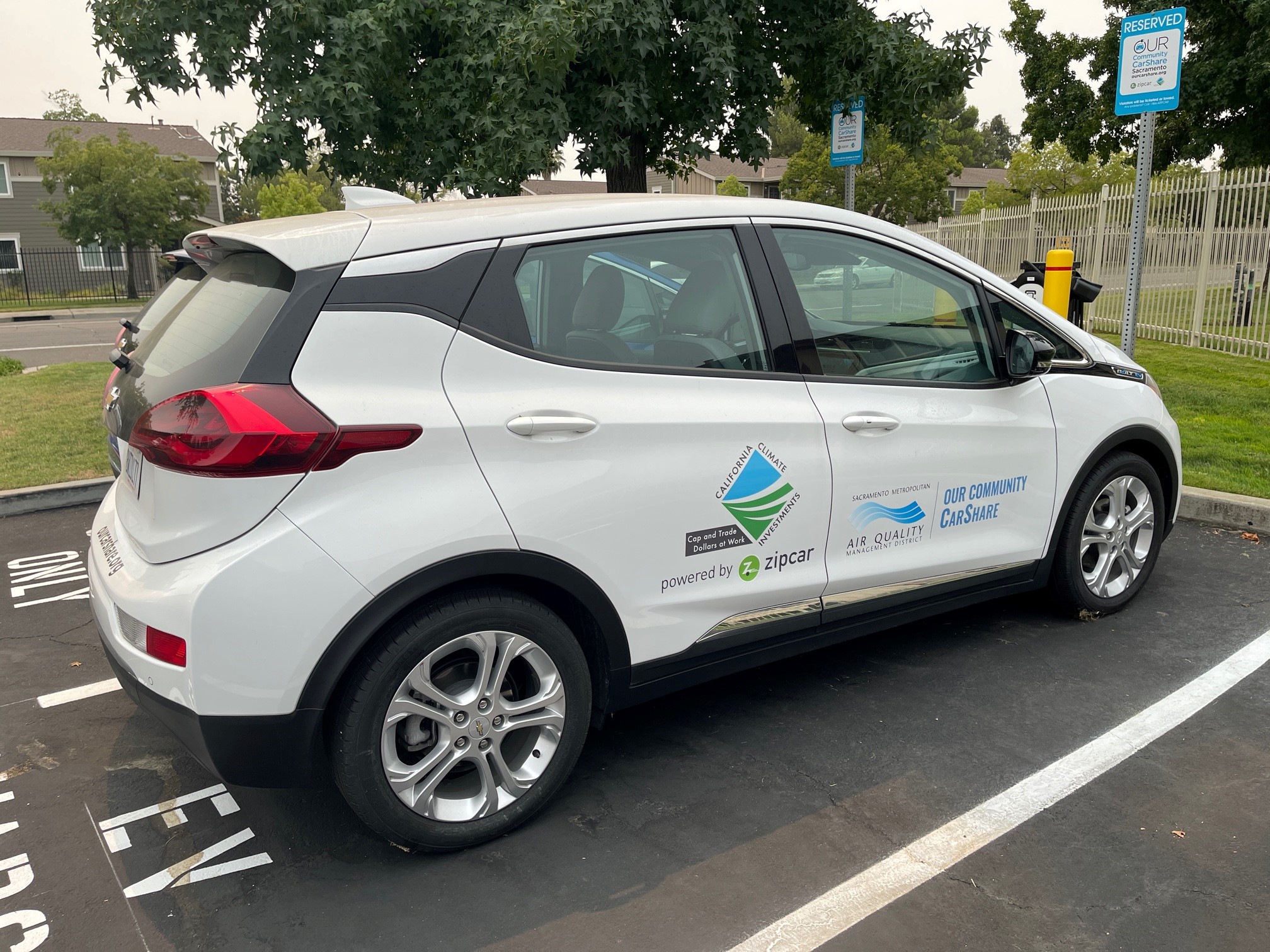 Side and rear view of parked white Chevy Bolt with Our Community Carshare logo