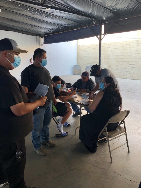Outreach event in which participants gather around a table taking surveys and wearing COVID-19 masks