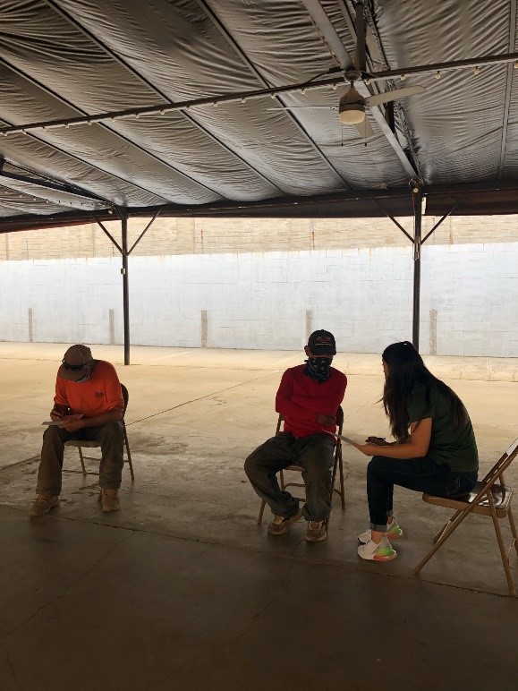 Indoor outreach event in which 3 participants sit in metal chairs taking a survey and wearing COVID-19 masks