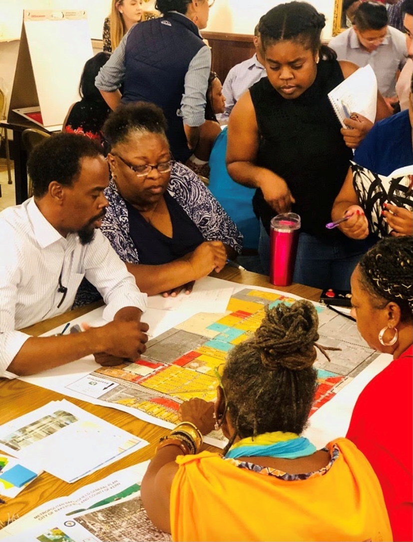 Community residents participating in a mapping exercise at an outreach event. Residents are seated at a table and adding notes and features to a map.