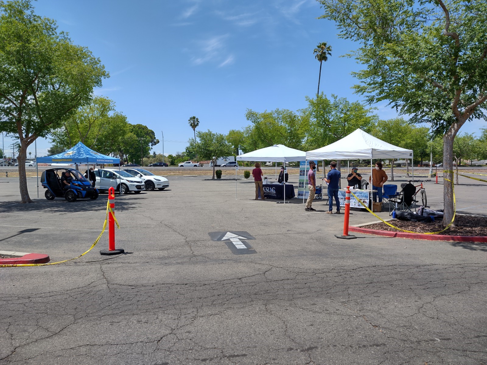Outdoor pop-up event with 3 easy up tents, electric vehicles on display, and event participants 