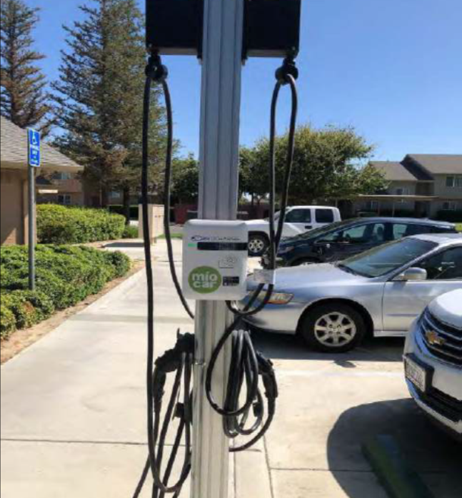 Miocar charging station installed in a site parking lot where other cars are parked. 