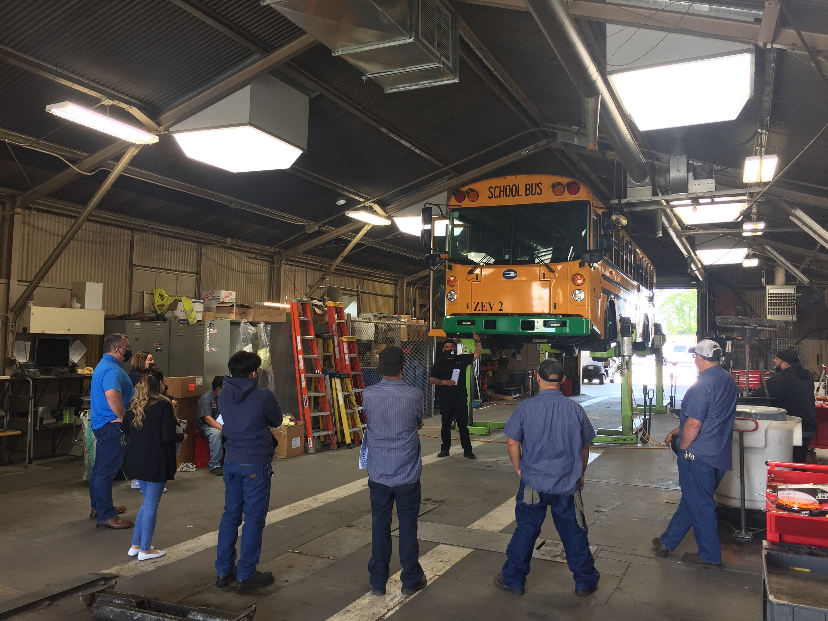 An electric school bus raised up in repair shop for educational discussion with SU District staff and students 