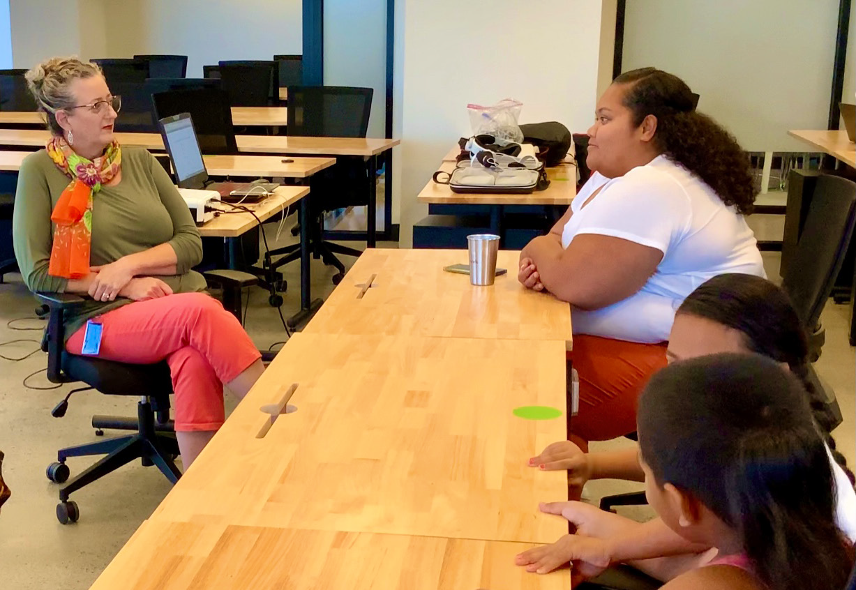 Virtual reality focus group with 3 participants, 1 adult and 2 children, and a facilitator, all sitting at a banquet style table 