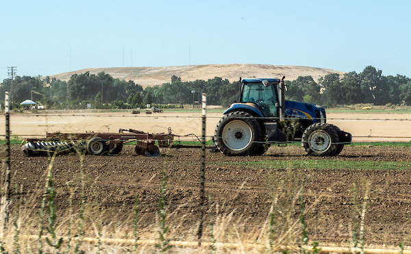 A New Holland tractor with a Krause disc harrow attached sits on farmland 