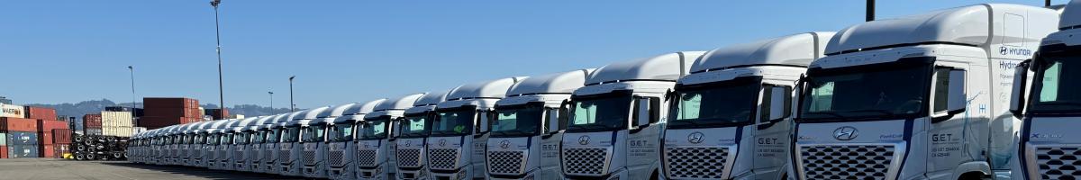 an image of 30 class 8 fuel cell electric trucks in a line viewed from at an angle, blue sky in background