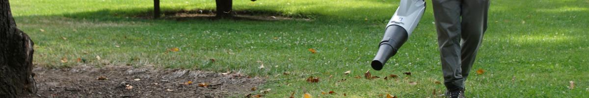  A landscaper using a leaf blower to blow leaves in a grassy area.