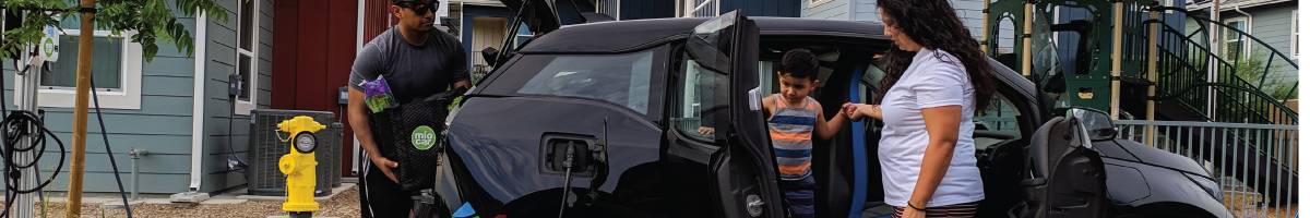 Family unloading groceries from a zero-emission vehicle plugged into a charger in front of a home