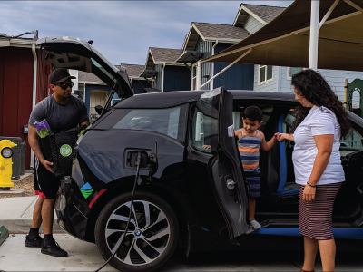 Family unloading groceries from a zero-emission vehicle plugged into a charger in front of a home