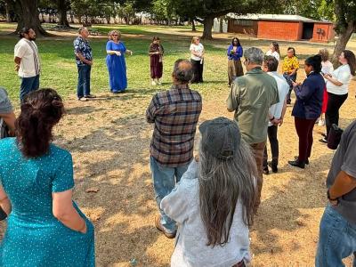 A group of people gathered in a park listening to a presenter. 